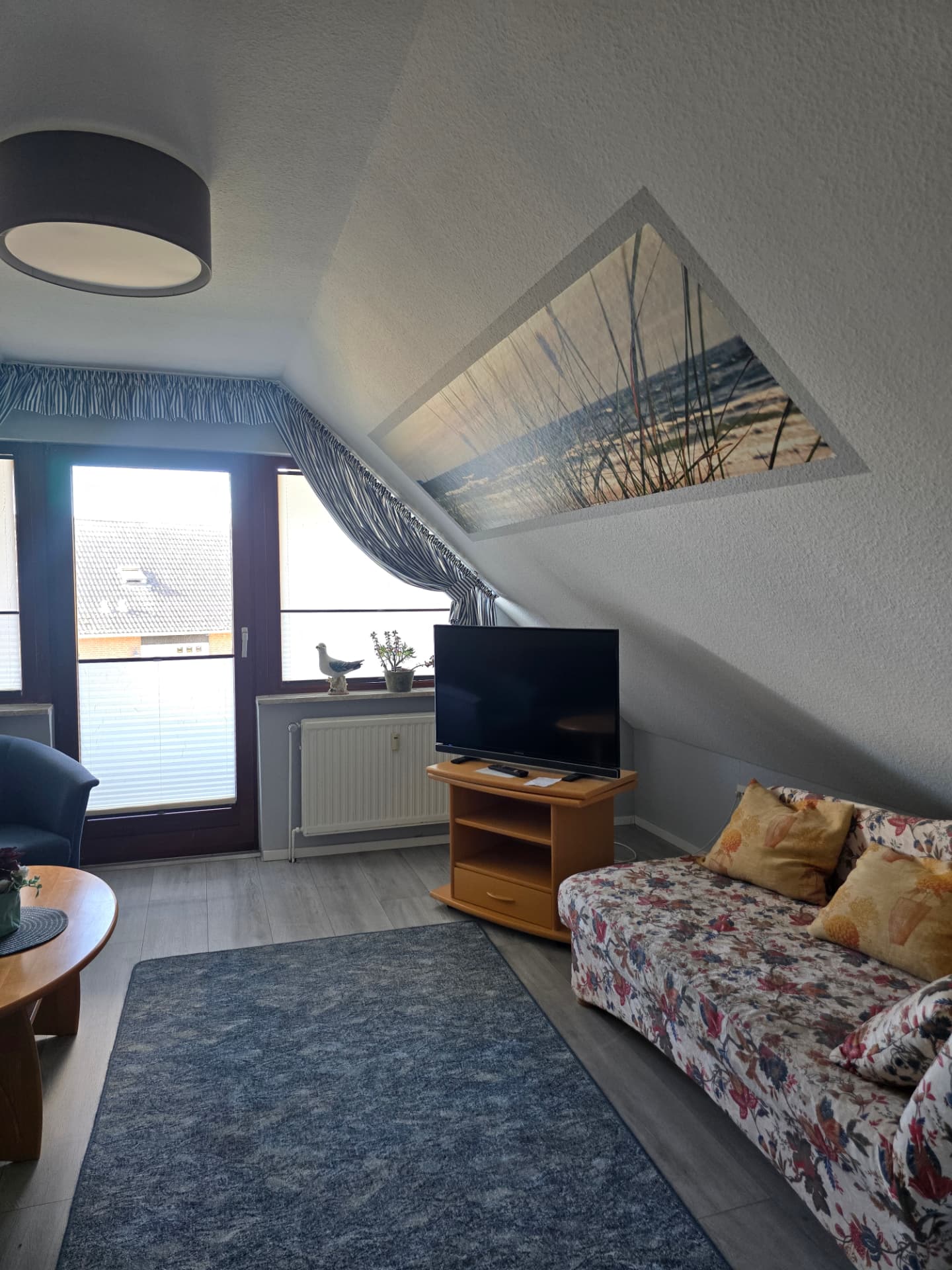 Wohnzimmer mit TV, Blumencouch und Strand-Wandbild unter der Dachschräge