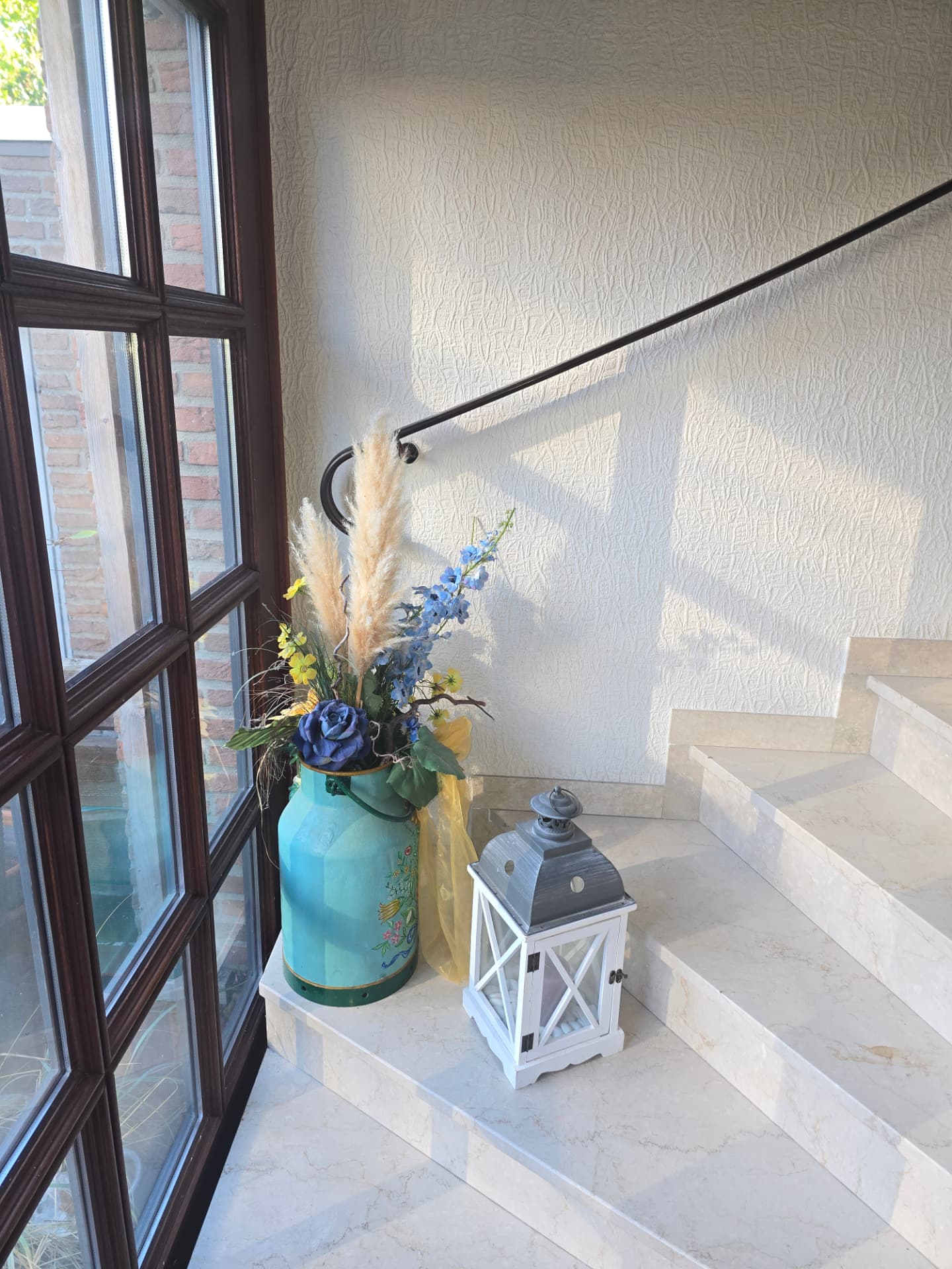 Steintreppe mit Geländer, blauer Milchkanne mit Blumen und Laterne im Eingangsbereich