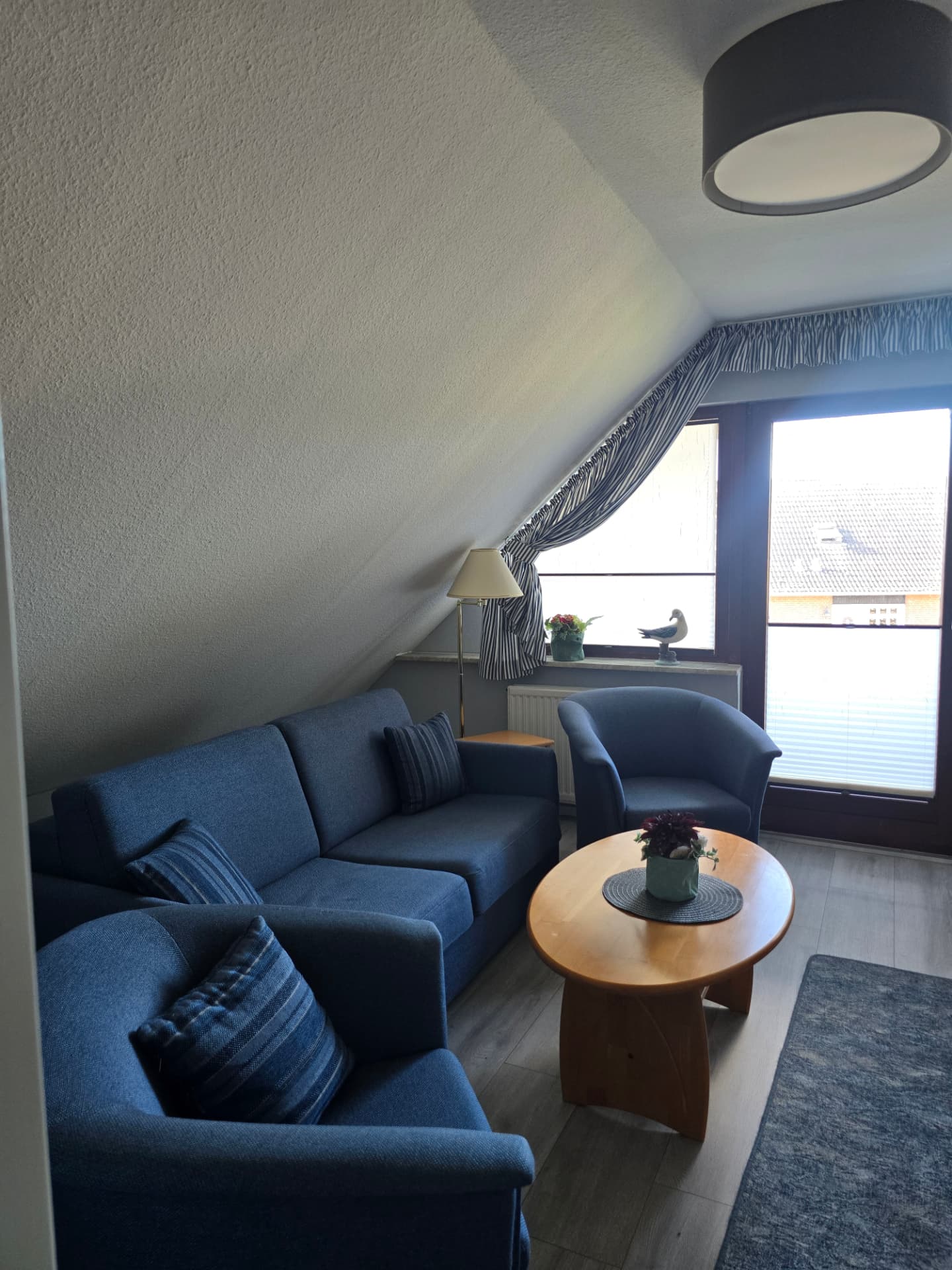 Wohnbereich mit blauer Couch, Sesseln und Blick zur Balkontür im See Adler