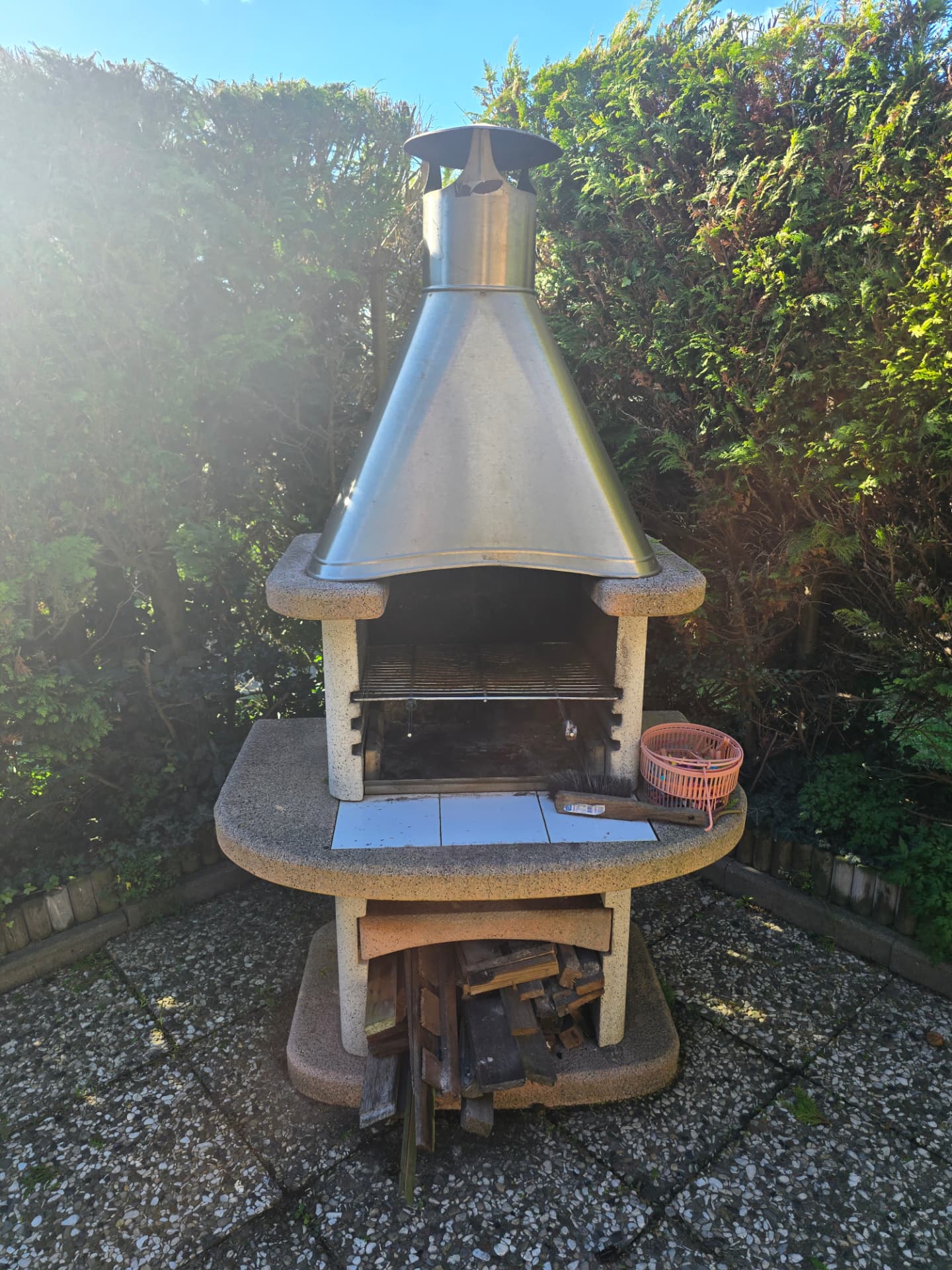 Gartengrill mit Edelstahlkamin zwischen grünen Hecken